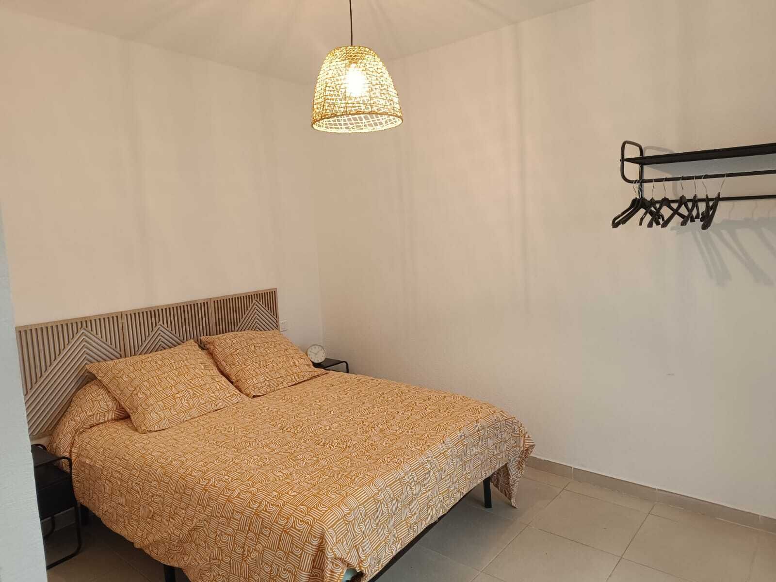 Un dormitorio con una cama, una lámpara colgante y un perchero.