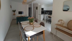 A modern kitchen with white cabinets, a microwave, and a sink. There is a dining area with a white table and chairs, and a TV on a stand. - Bright cocoon with private courtyard (Salses-le-Château)