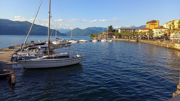 Un puerto deportivo con varios veleros amarrados, un paseo marítimo y edificios a lo largo de la costa.