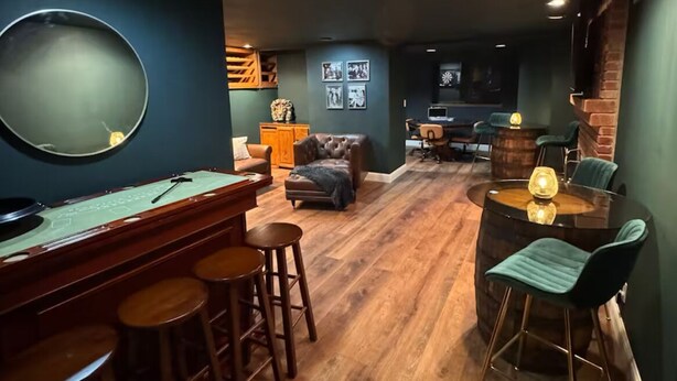 A dimly lit room with a pool table, bar stools, and a dining area with a table and chairs.