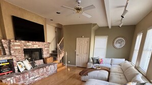 A spacious living room with a brick fireplace, a large sectional sofa, and a ceiling fan.