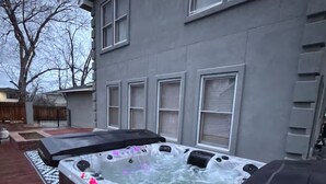 A hot tub in a backyard with a gray house in the background.