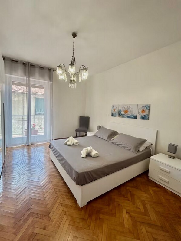 A bedroom with a large bed, a chandelier, a chair, and artwork on the wall.