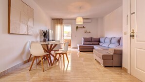A modern living room with a sofa, a dining table with chairs, and a large abstract painting on the wall. - Anna del Mar | Coastal Boho (San Luis de Sabinillas)