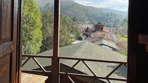 A room with a large window offering a view of a mountainous landscape and a building with a red roof. - Olympos Talara (Kumluca)