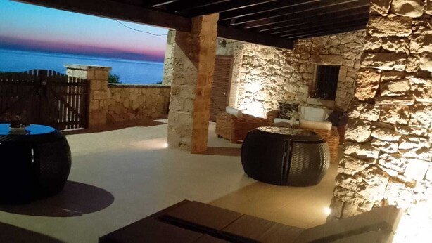 An outdoor patio with stone walls, two large black planters, and a view of the sea.