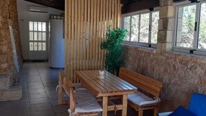A wooden table with benches, a blue sofa, and a potted plant in a stone-walled room with large windows.