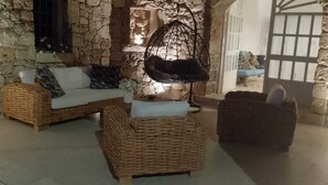 A stone-walled room with wicker furniture, including a sofa and two poufs.