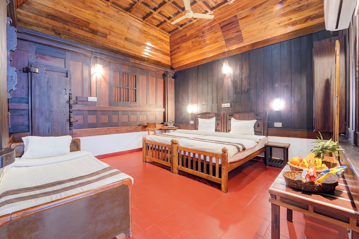 Una habitación con suelo de madera, dos camas, una mesita con fruta y un ventilador de techo.