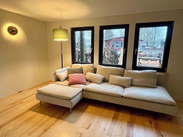 Una sala de estar moderna con un sofá modular, una lámpara de pie y ventanas amplias que ofrecen vistas al exterior.