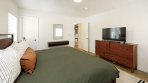 Un dormitorio con una cama, un televisor sobre un tocador de madera, un espejo en la pared y una puerta que da a un armario.