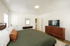 Een slaapkamer met een bed, een televisie op een houten dressoir, een spiegel aan de muur en een deur naar een inloopkast.
