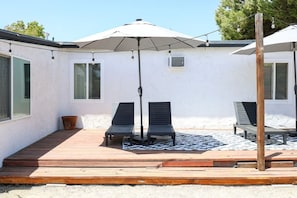 Un área de patio con dos sillones de descanso, una sombrilla grande y una terraza de madera.