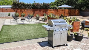 Un patio trasero con una parrilla, un pequeño césped y mobiliario exterior.