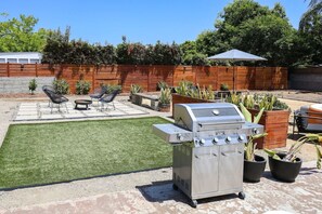 Een achtertuin met een barbecue, een gazon en tuinmeubilair.