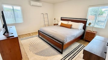 A bedroom with a bed, bedside tables, a desk, an air conditioner, and a window.