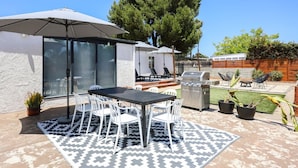 Un patio al aire libre con mesa y sillas, una parrilla y un gran paraguas.