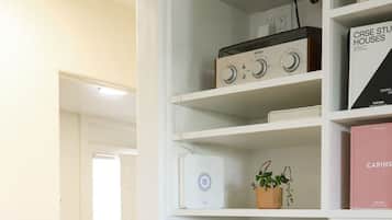 A white interior with a bed, a white shelf unit containing a radio, books, and a plant.