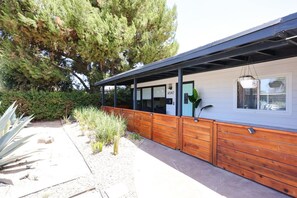 Een modern gebouw met een overdekte veranda, een houten hek en een cactuss in de voorgrond.