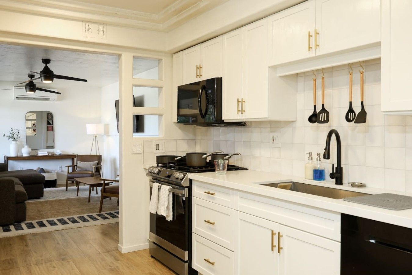 A modern kitchen with white cabinetry, a black stove, and a microwave. There is a dining area with a table and chairs visible through an open doorway.