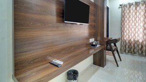 Un salon moderne avec un meuble TV en bois, un téléviseur à écran plat, une télécommande et une petite table sur laquelle se trouvent une boîte de mouchoirs et des lunettes.