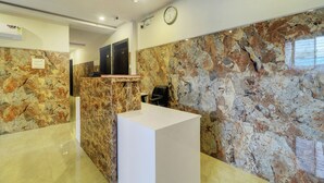 Un espace d’accueil avec un mur en marbre, un comptoir de réception et une horloge au mur.