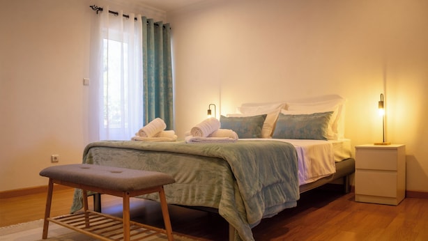 Une chambre à coucher avec un lit, des tables de chevet, un banc et une fenêtre avec des rideaux.
