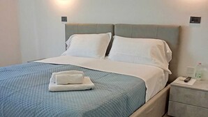 A neatly made bed with a blue bedspread and white pillows, a bedside table with a remote control, and two wall-mounted lights. - Hotel Edelweiss Mantova (Castel d'Ario)