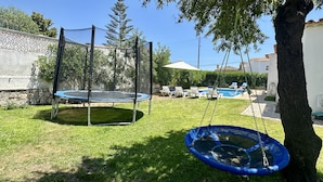 A backyard with a trampoline, a swing, and a pool.