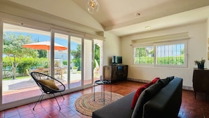 A spacious living area with a large sliding glass door leading to an outdoor patio, a comfortable sofa, a television on a cabinet, and a small round rug.