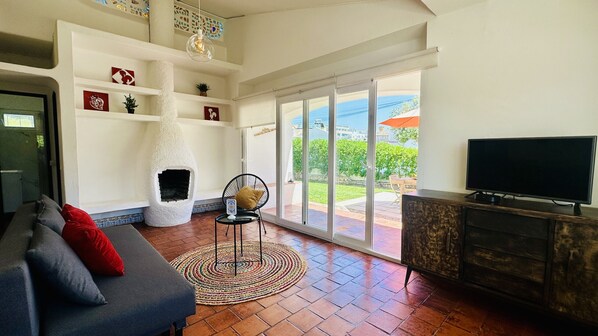 A living room with a fireplace, a sofa, a television, and a view of the outdoors.