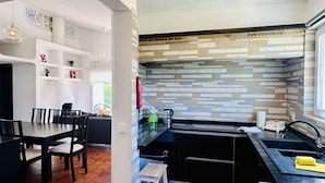 A modern kitchen with a black countertop, a sink, and a backsplash with a geometric pattern. There is a dining area with a table and chairs, and a small stool.