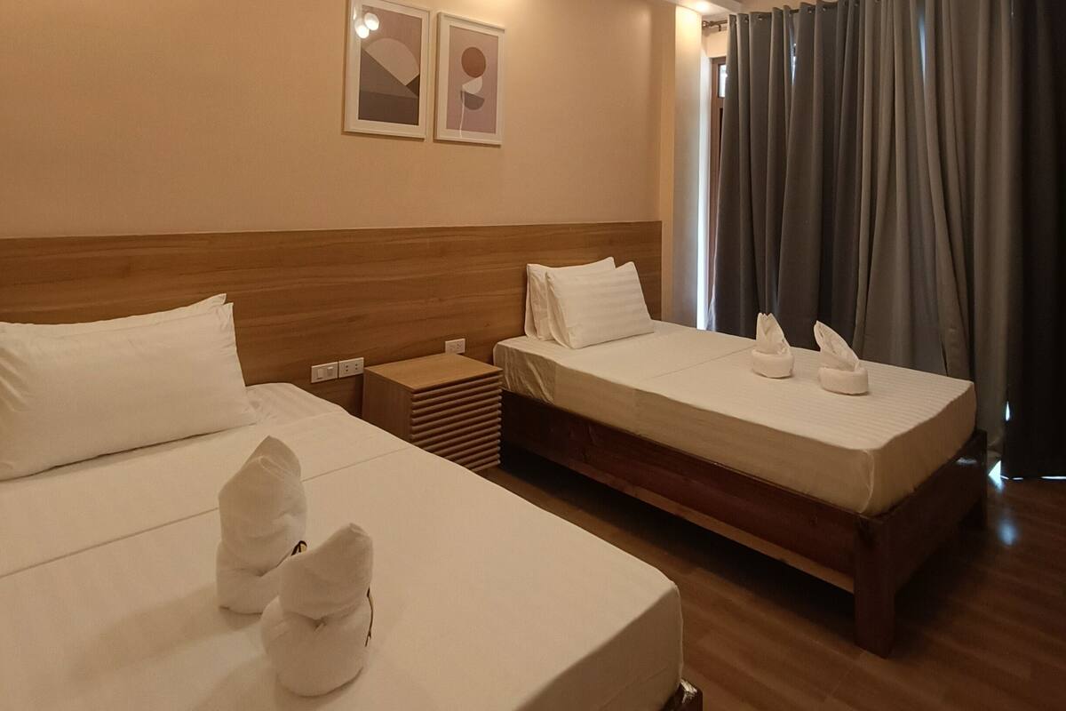 A hotel room with two beds, a wooden headboard, a nightstand, and a ceiling light fixture.