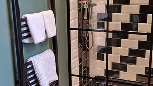 Een badkamer met een douche met glazen wand, een handdoekrek met twee handdoeken en een betegelde muur met een zwart-wit patroon.
