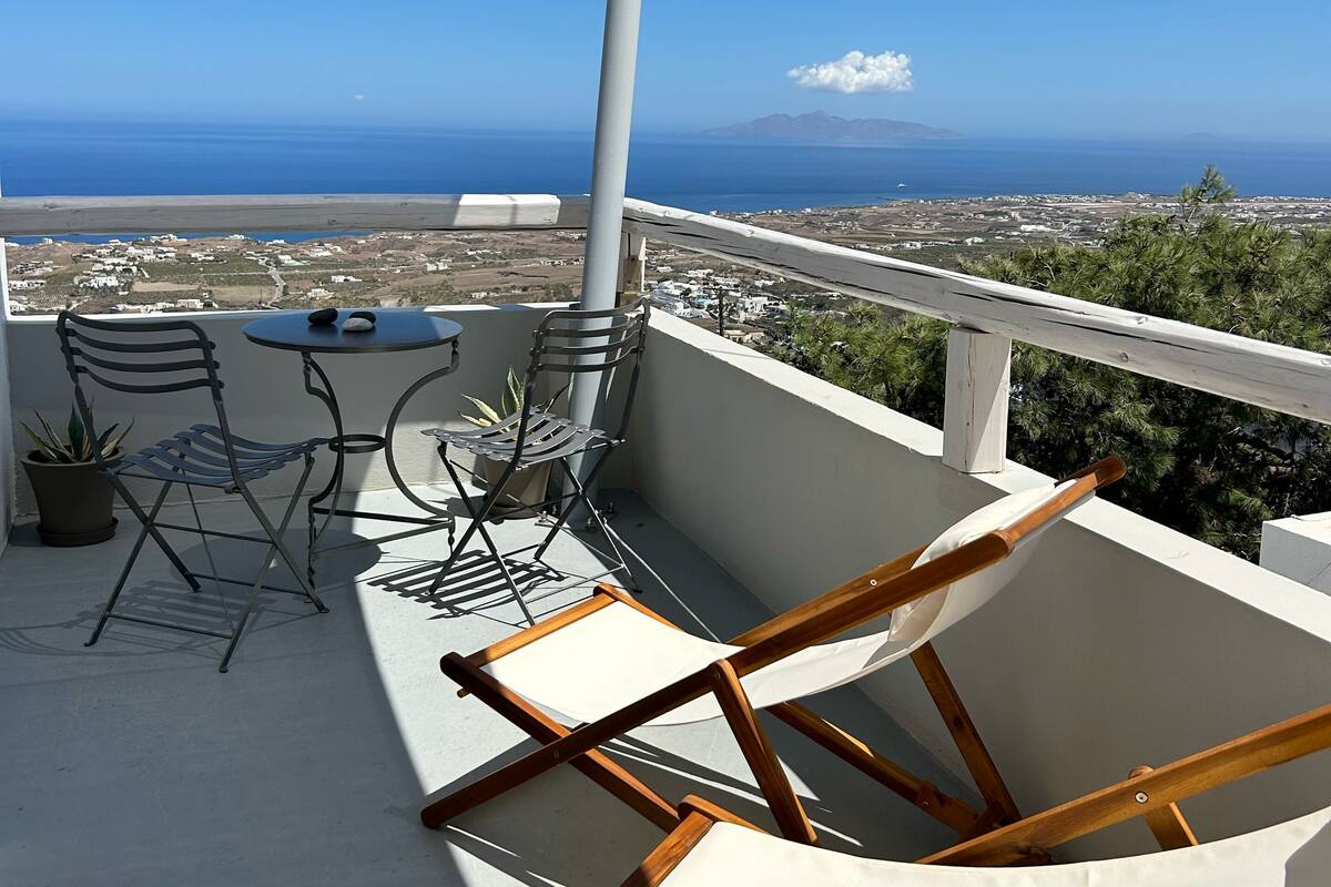 A balcony with a view of the sea, a table, two chairs, and a potted plant.