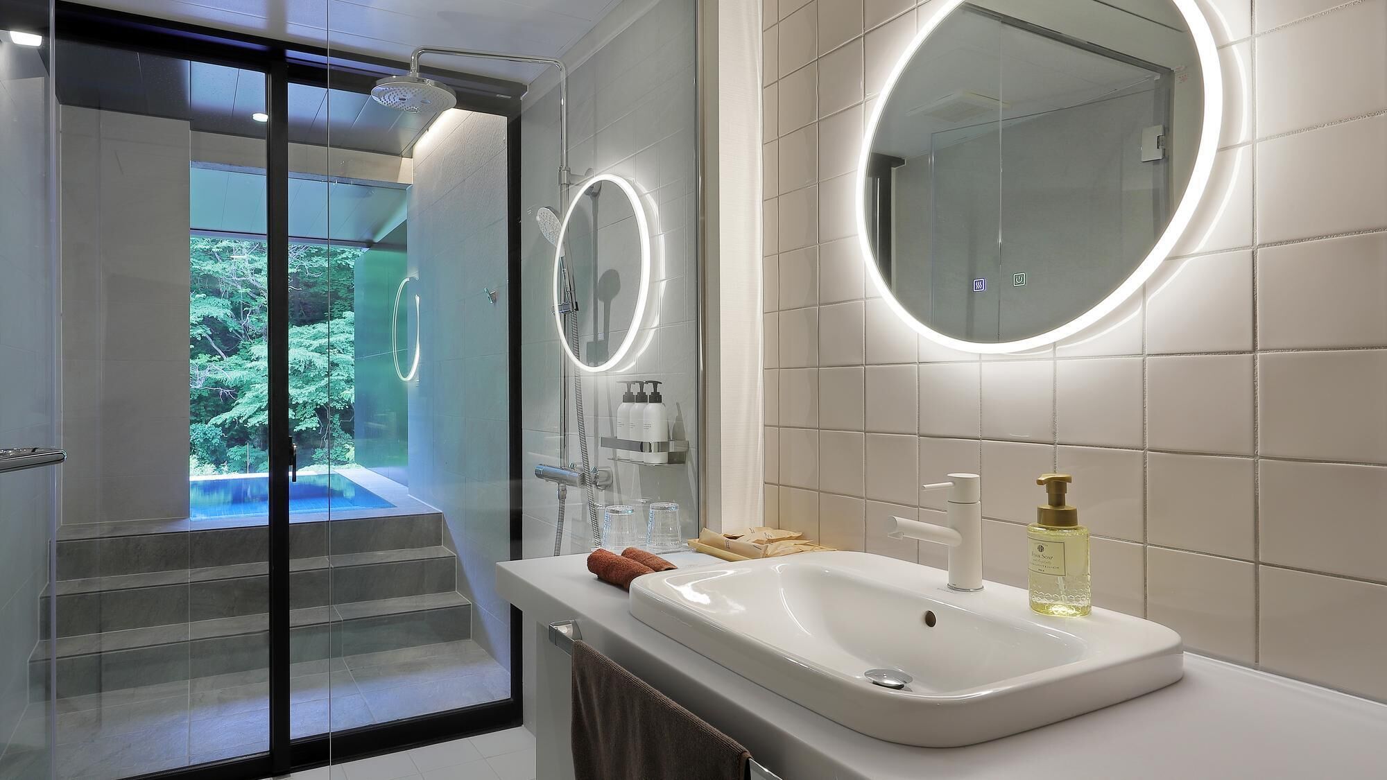 A modern bathroom with a glass shower enclosure, a large mirror, and a sink with toiletries.