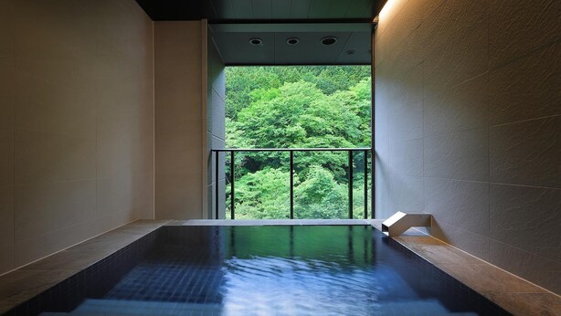 A spa room with a view of a forest through a glass window. - KANOUYASHIMAONSEN (Nakanojo)