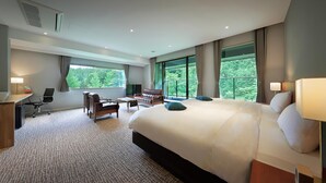 A modern hotel room with a large bed, a desk, a chair, and a sofa. There are large windows with a view of trees. - KANOUYASHIMAONSEN (Nakanojo)