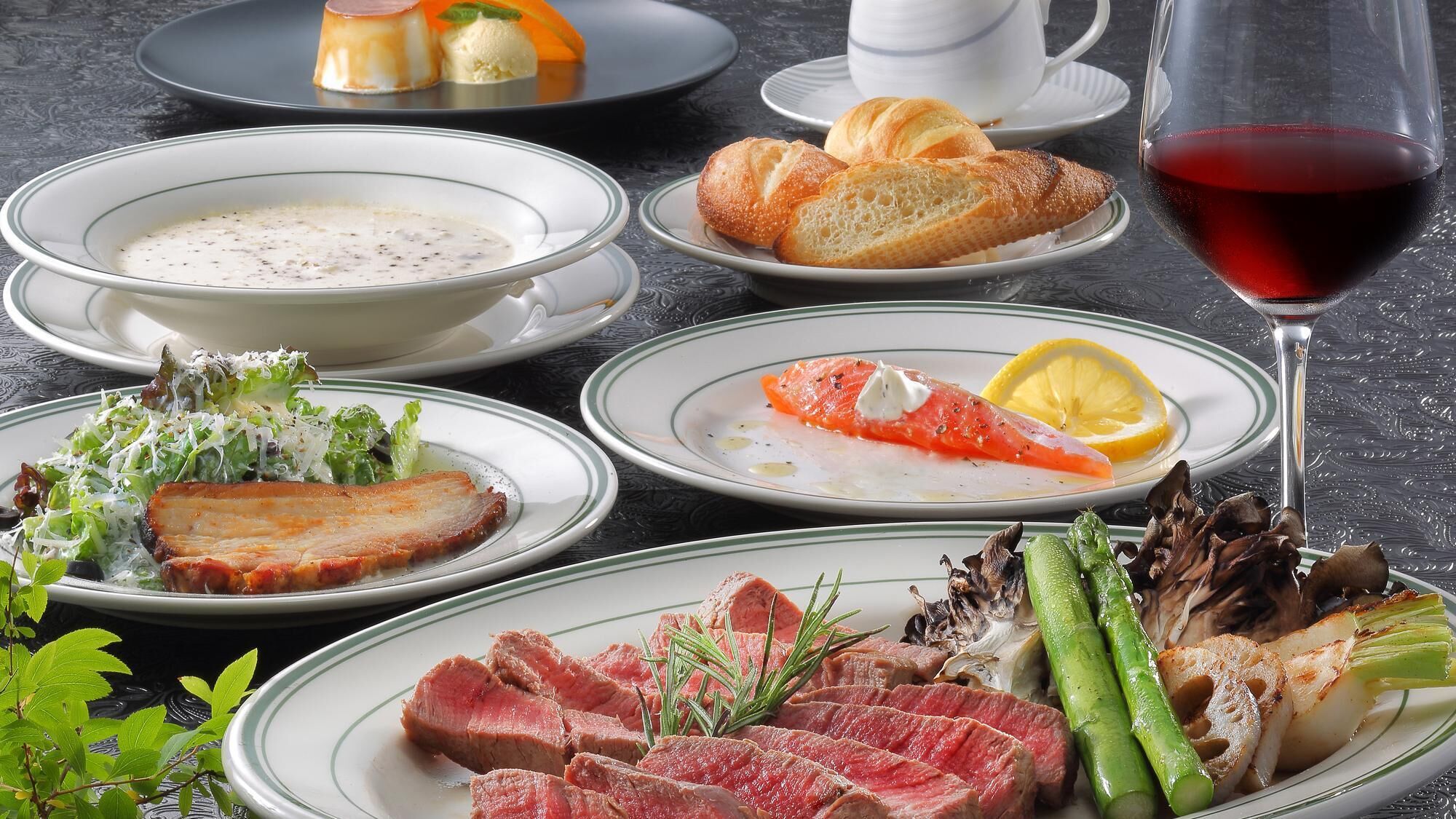 A table set with various dishes including soup, bread, and meat, along with a glass of red wine.