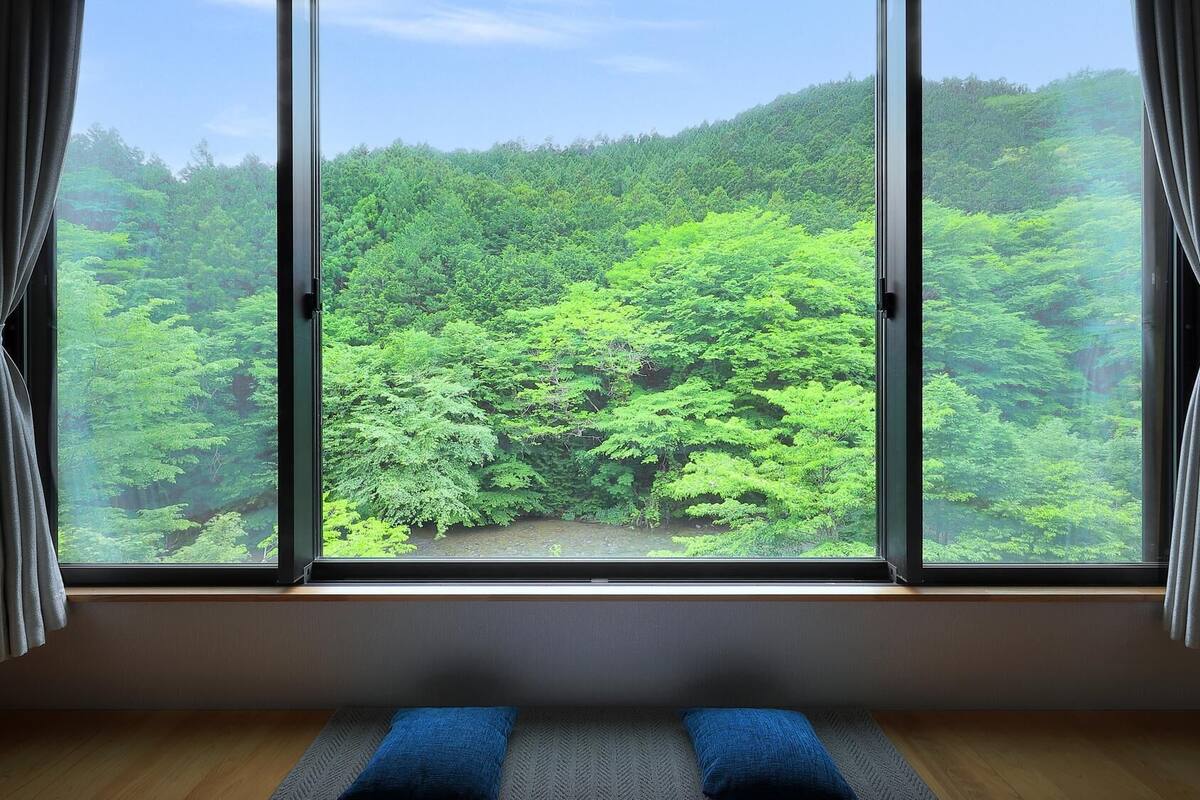 A room with a large window overlooking a dense forest.