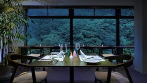 A dining table set for four with a view of a dense forest through large windows. - KANOUYASHIMAONSEN (Nakanojo)