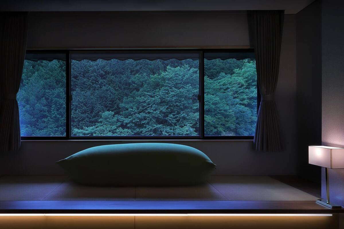 A bedroom with a large window, a bedside lamp, and a pillow on a bed.