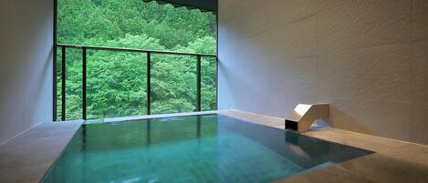 A modern indoor swimming pool with a view of a dense forest through large windows.
