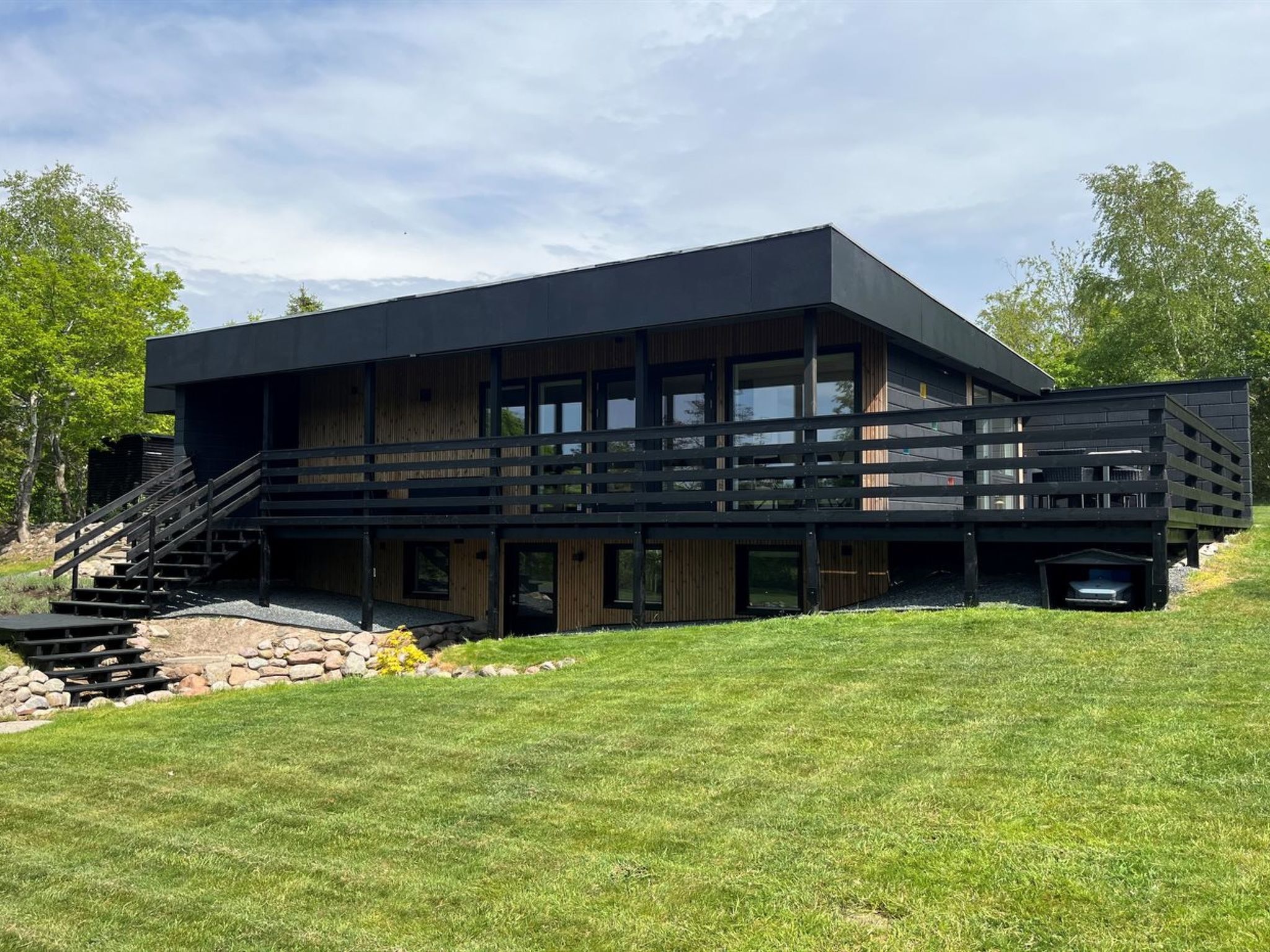 Un bâtiment moderne à deux étages, doté d’un toit plat, de grandes fenêtres et d’une terrasse en bois.