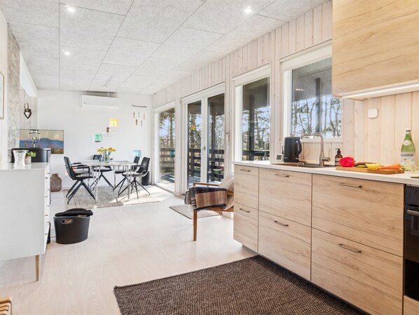 A modern kitchen with wooden cabinets, a dining area with a table and chairs, and large windows providing natural light.