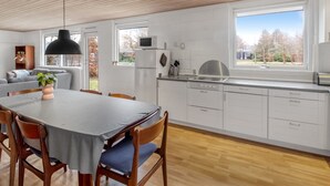 Una cocina moderna con armarios blancos, una mesa de comedor con sillas y un ventanal grande.
