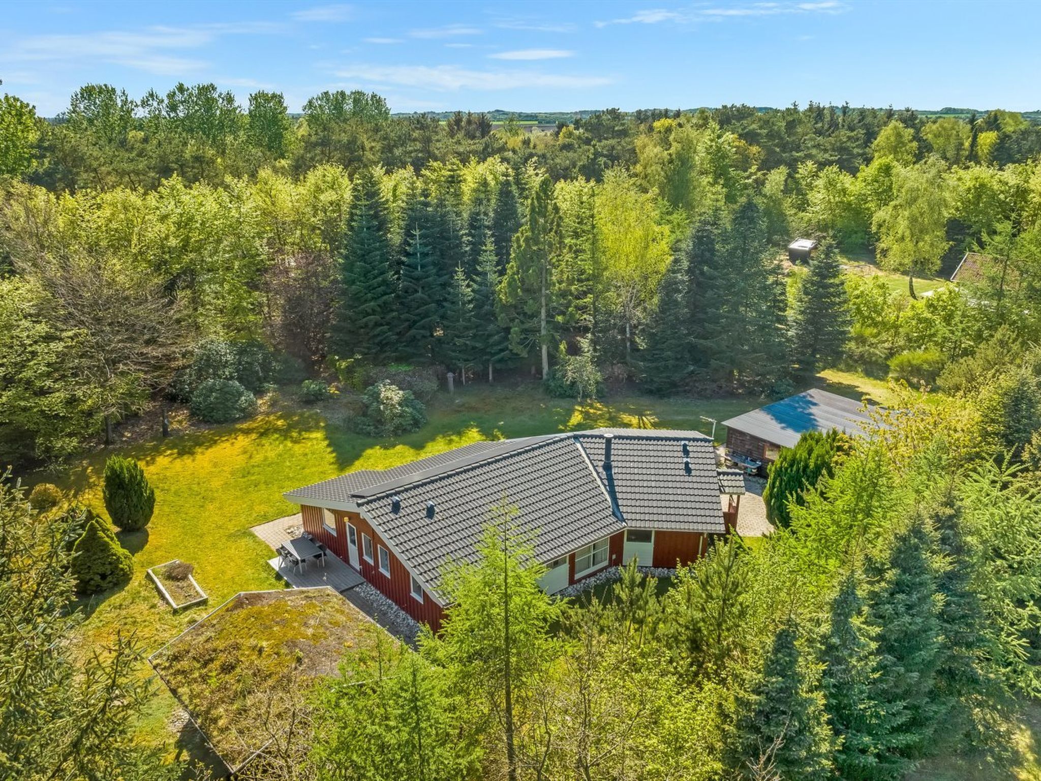 A modern house with a sloped roof, surrounded by dense forest.