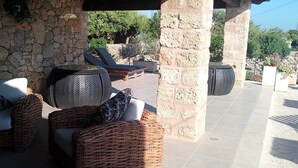 A covered outdoor seating area with wicker furniture and a stone wall backdrop.