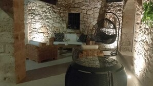 A stone-walled interior with wicker furniture, a hanging chair, and a barrel.