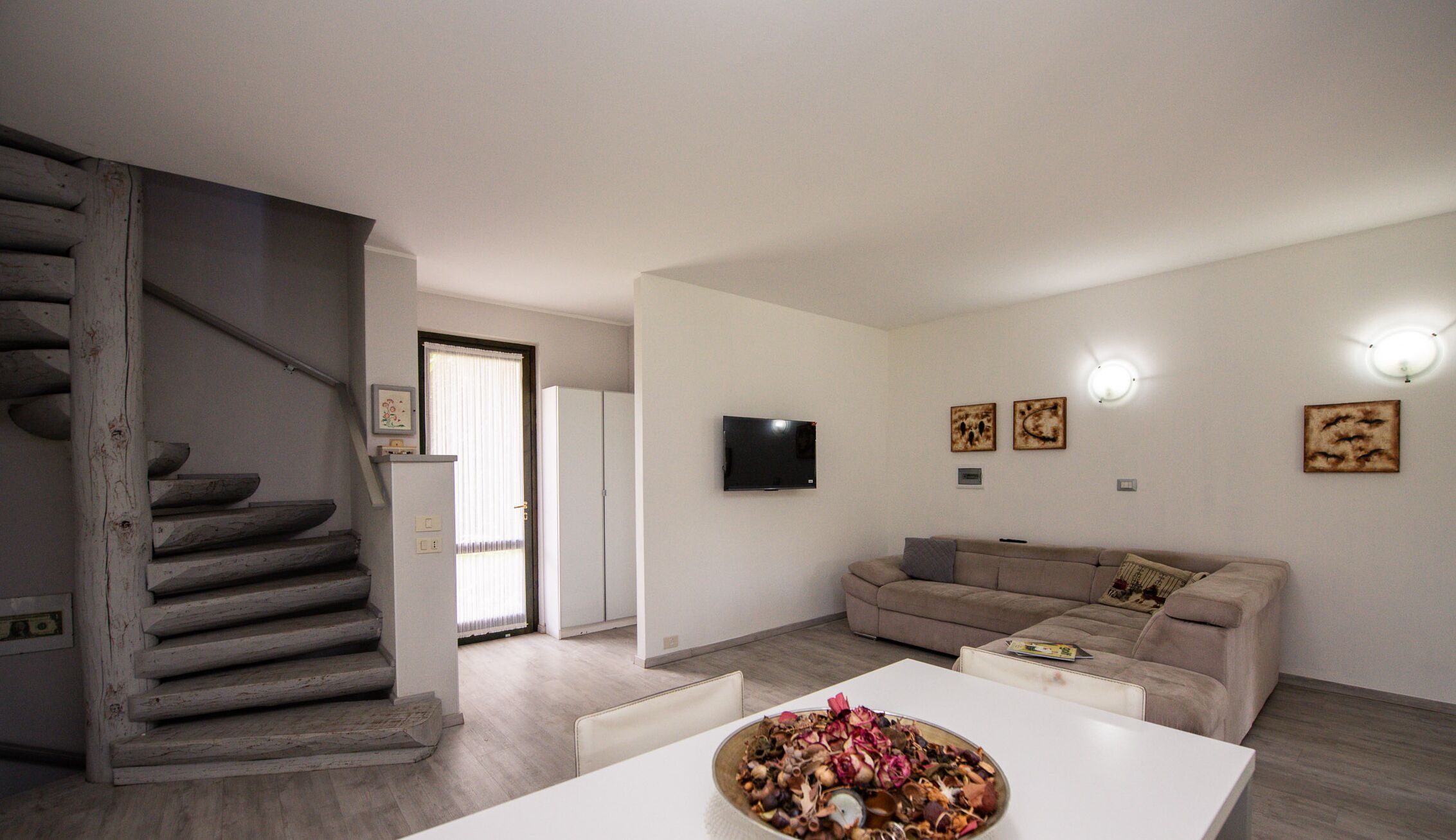 Una sala de estar moderna con una escalera, un televisor de pantalla plana y un comedor con un tazón de comida.